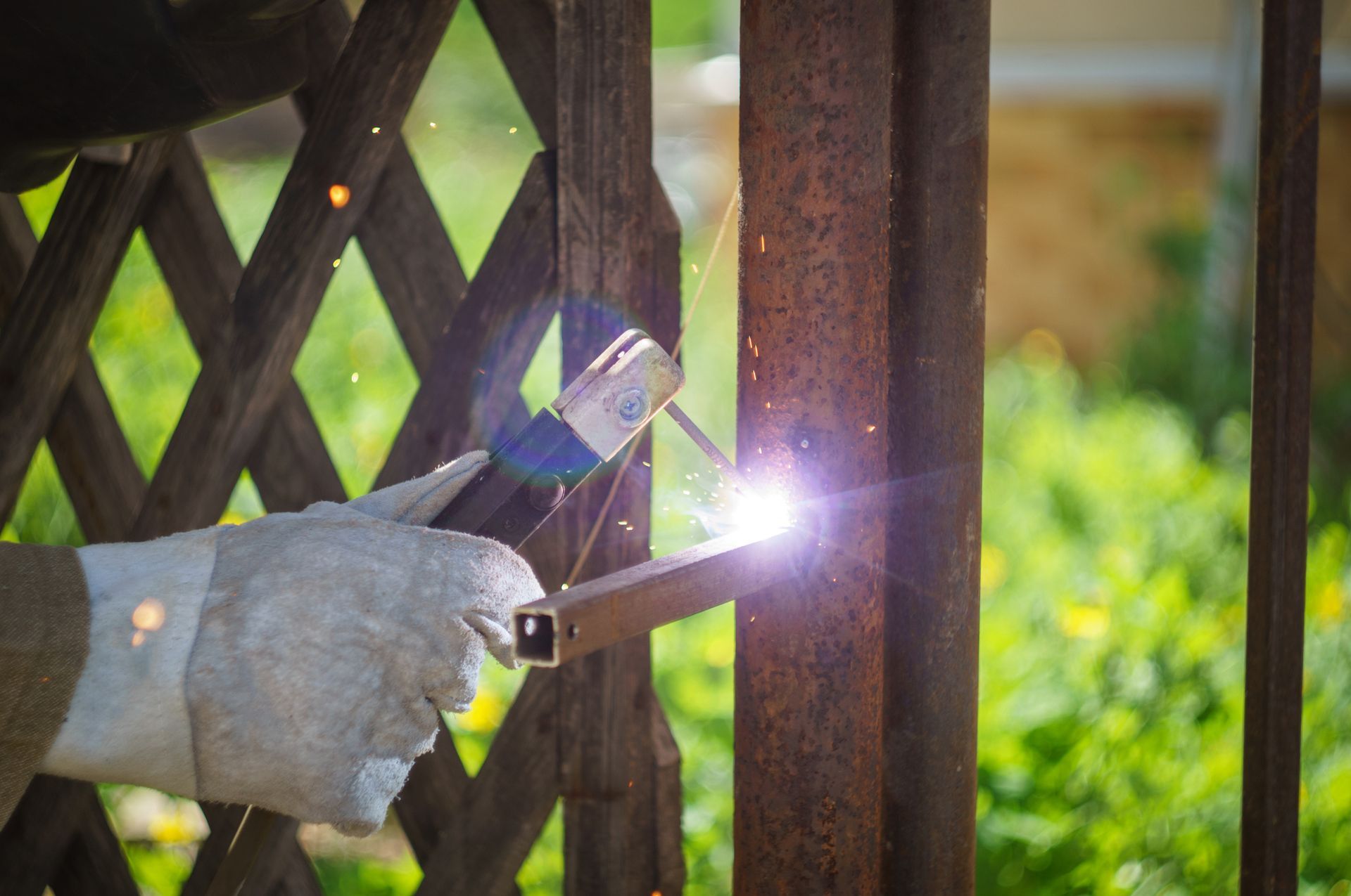 Gloved worker welding metal fence frame outdoors as bright sparks fly from the welding torch today.
