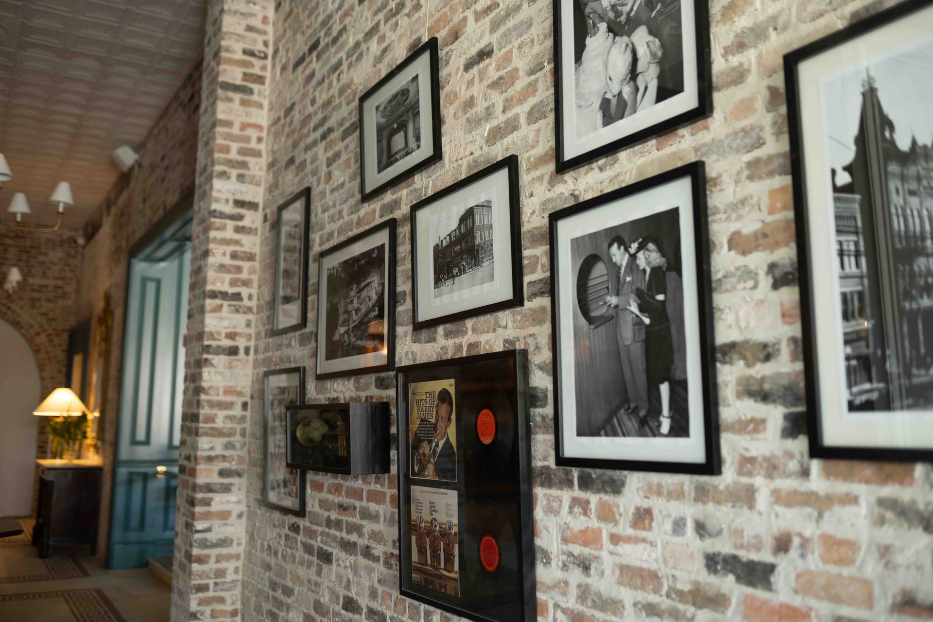 A brick wall in an indoor space displays several framed black-and-white photographs and a tall display case.