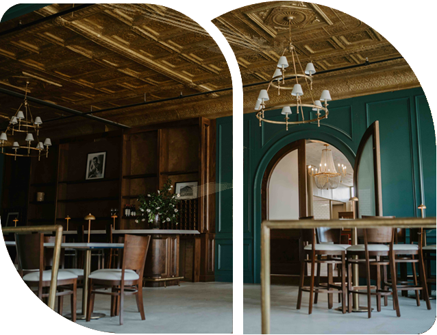 An elegant room with dark green walls, wood paneling, a gold patterned tin ceiling, and tiered chandeliers over tables.