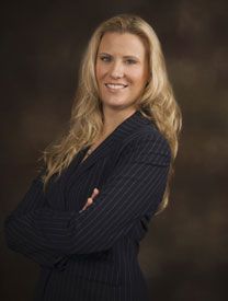 Studio portrait of a smiling woman in a dark pinstripe suit with arms crossed on a brown backdrop