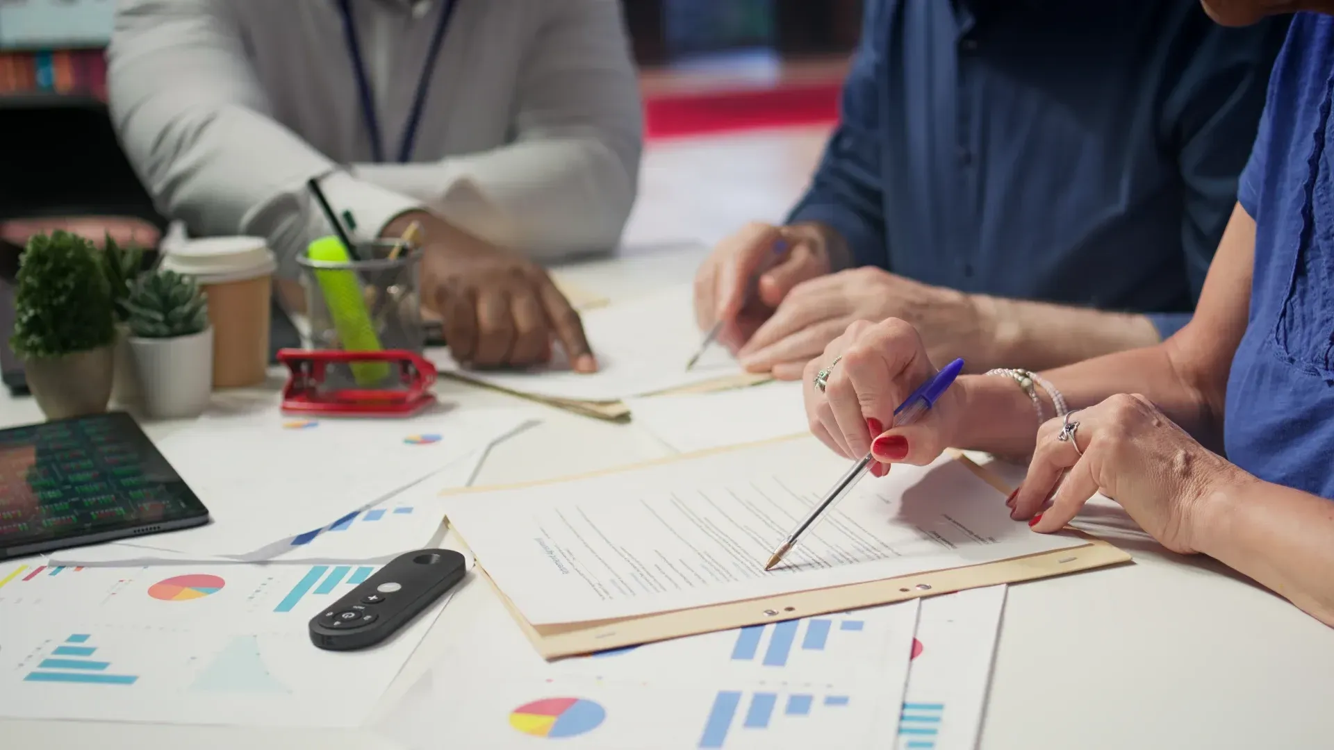 People collaborating at a desk with charts, documents, and pens during a meeting