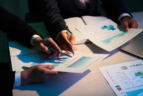 Hands reviewing printed charts and graphs around a table in a business meeting