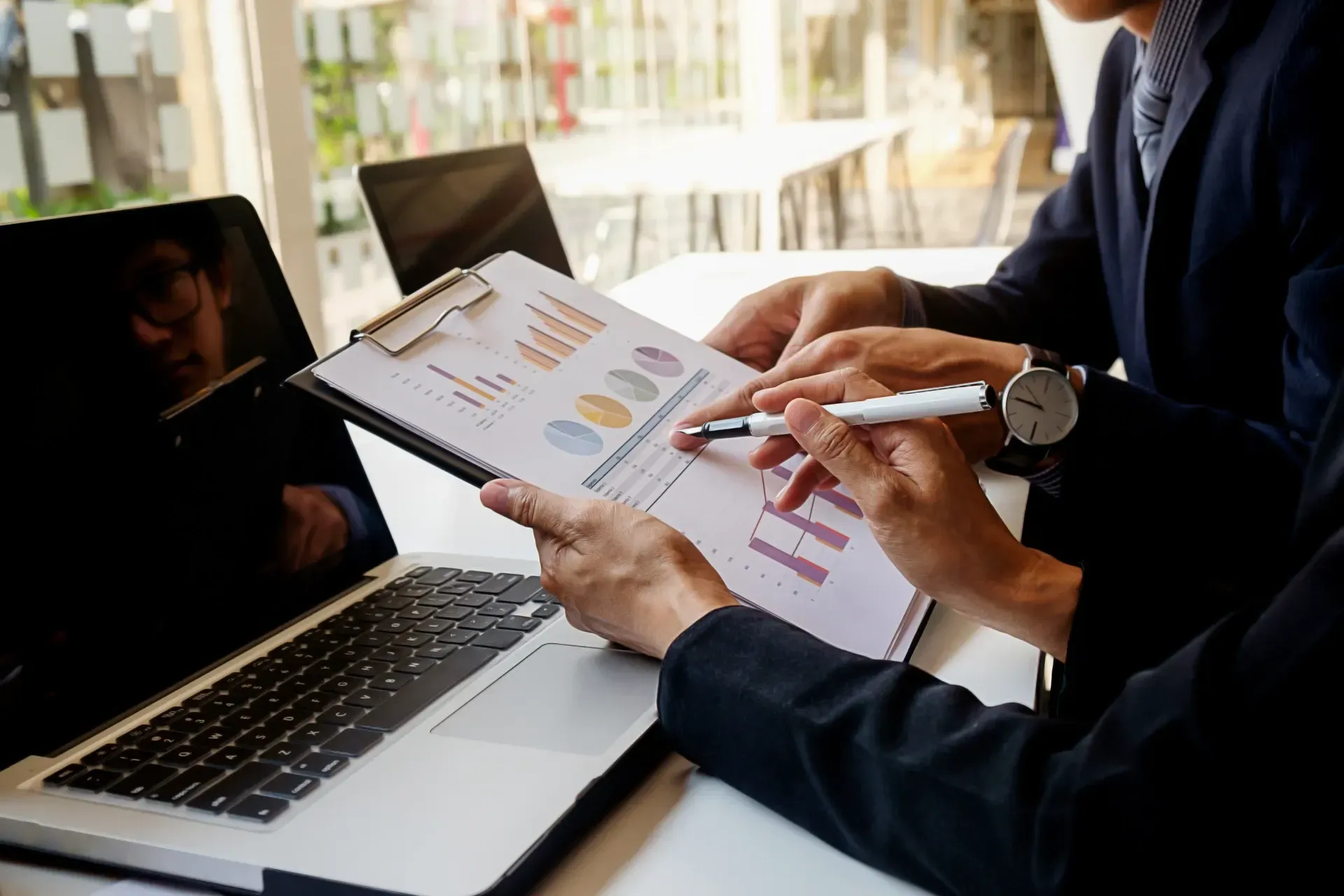 Two people review colorful charts and notes beside a laptop in a bright office meeting.
