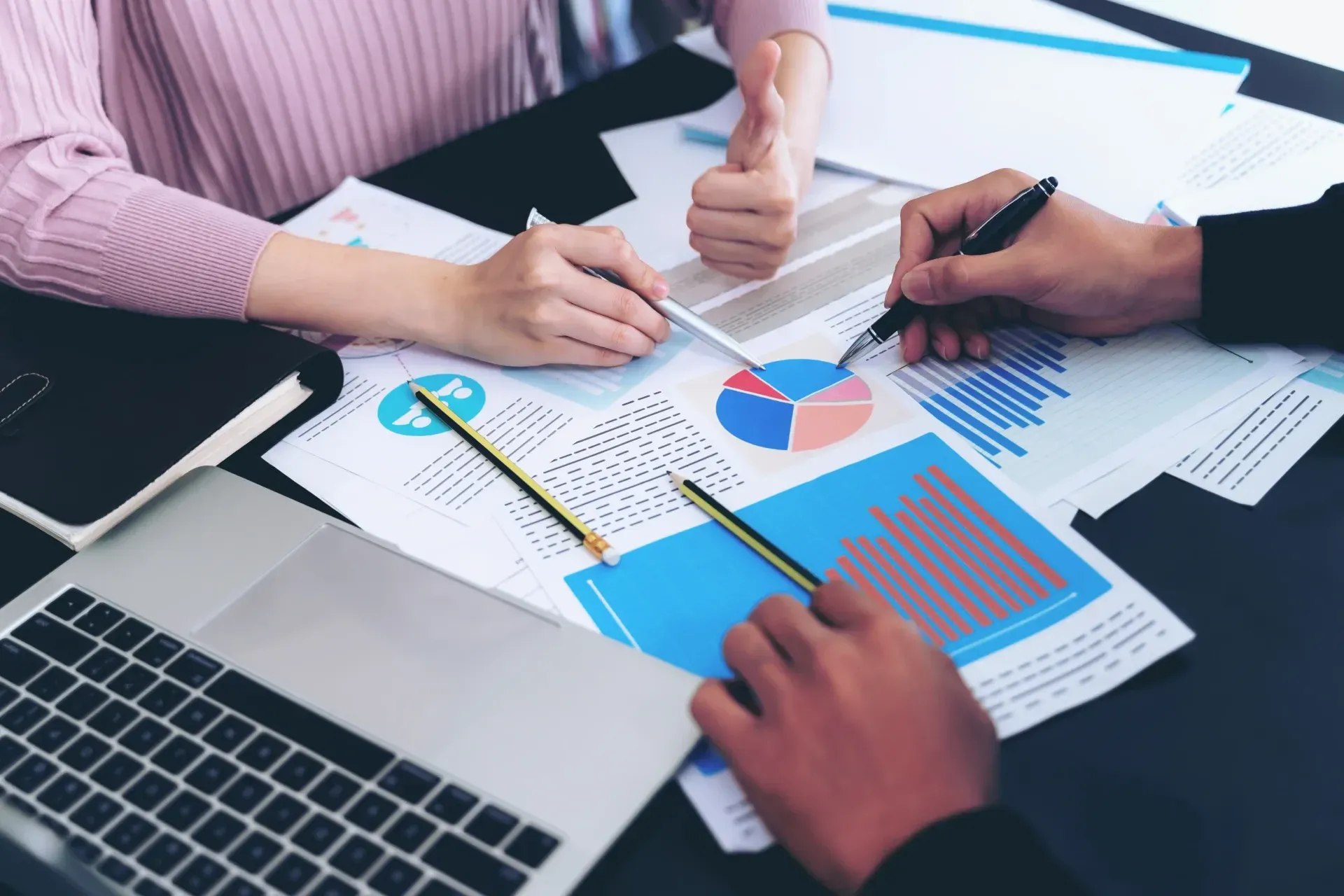 Hands reviewing colorful charts and graphs beside a laptop in a meeting