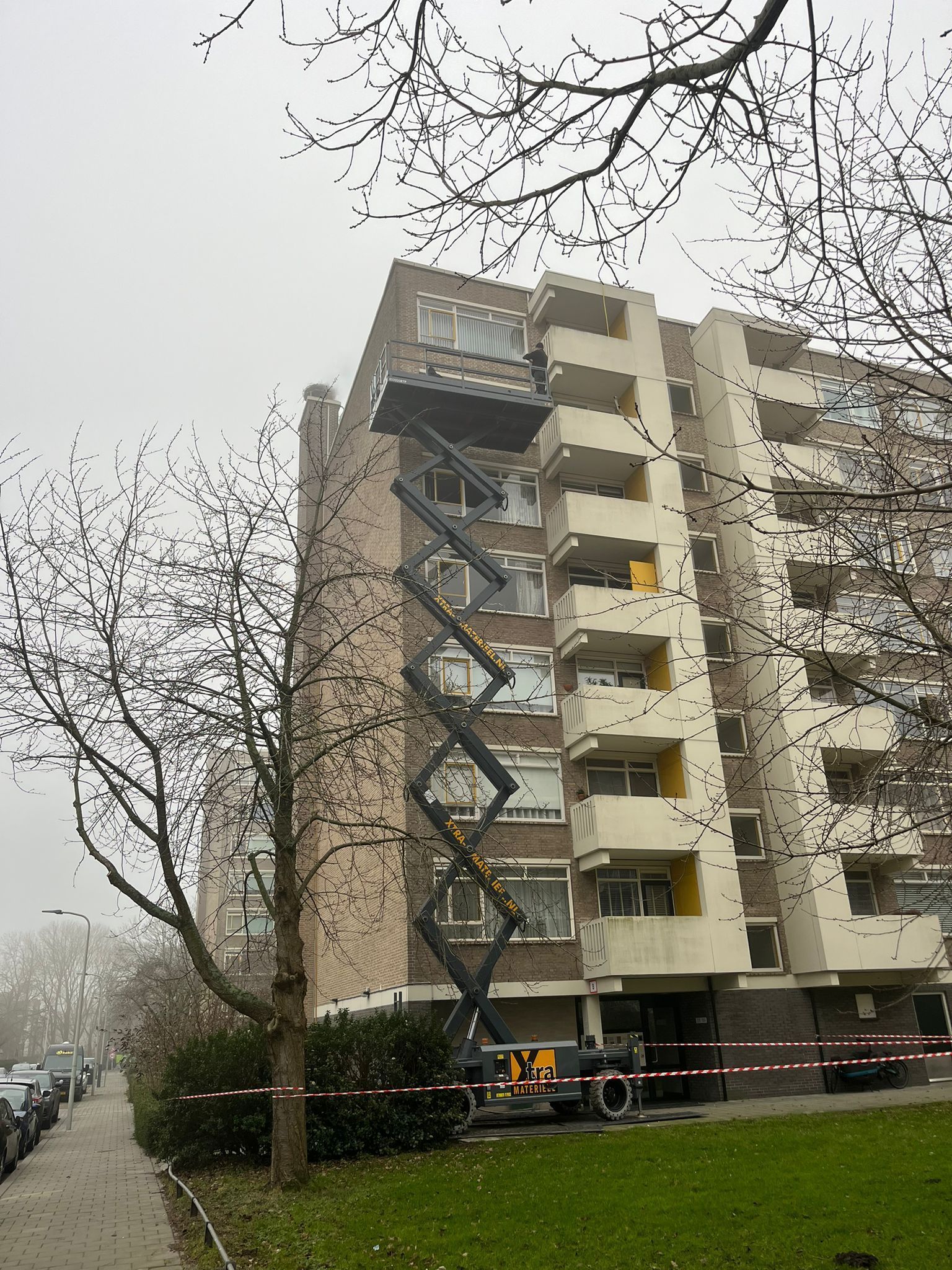 Een hoog appartementencomplex met een liftplatform; een lift brengt spullen naar een hogere verdieping.