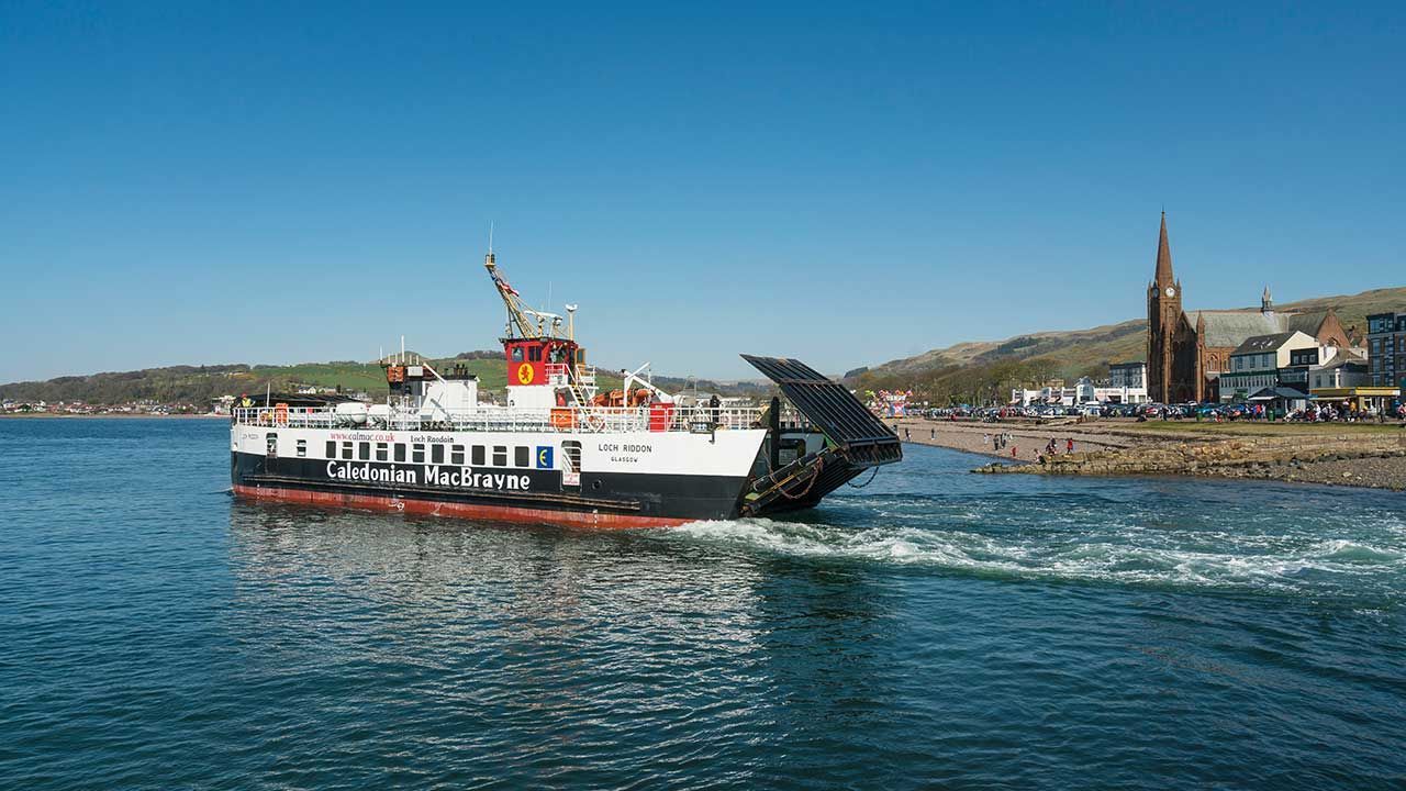 White ferry crossing blue water near a coastal town with a church spire in the background