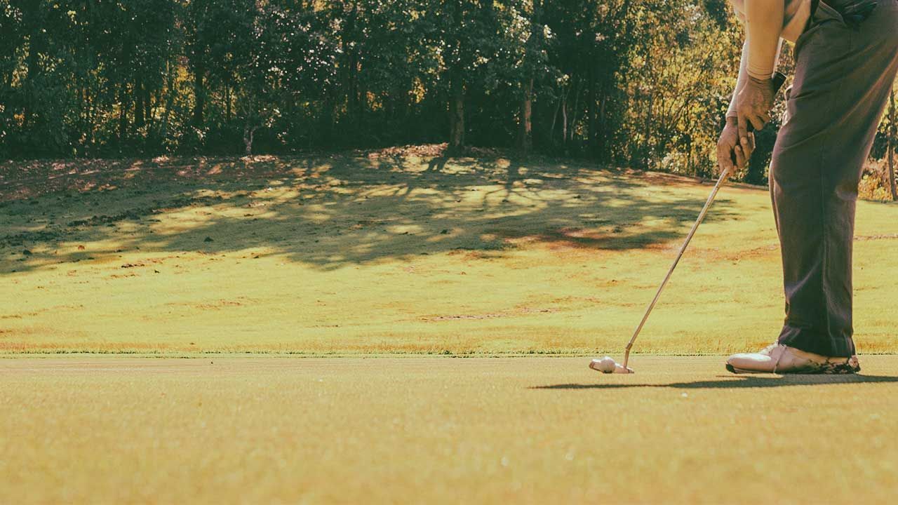 Golfer lining up a putt on a green, with trees in the background.