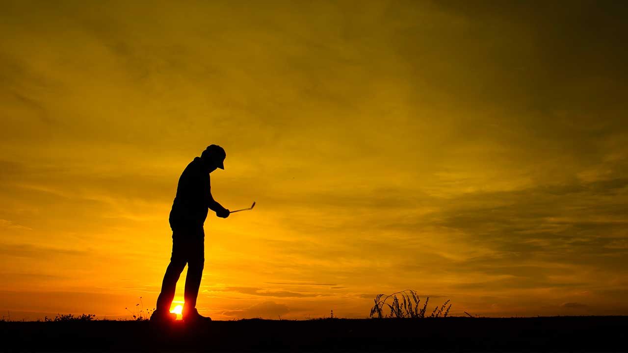 Silhouette of a person playing golf at sunset against a golden sky