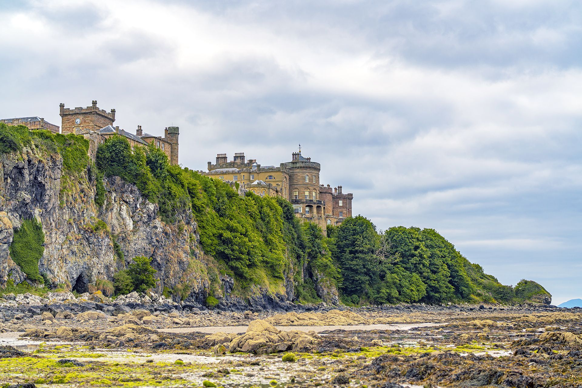 Stone castle on a green cliff above a rocky shoreline under a cloudy sky