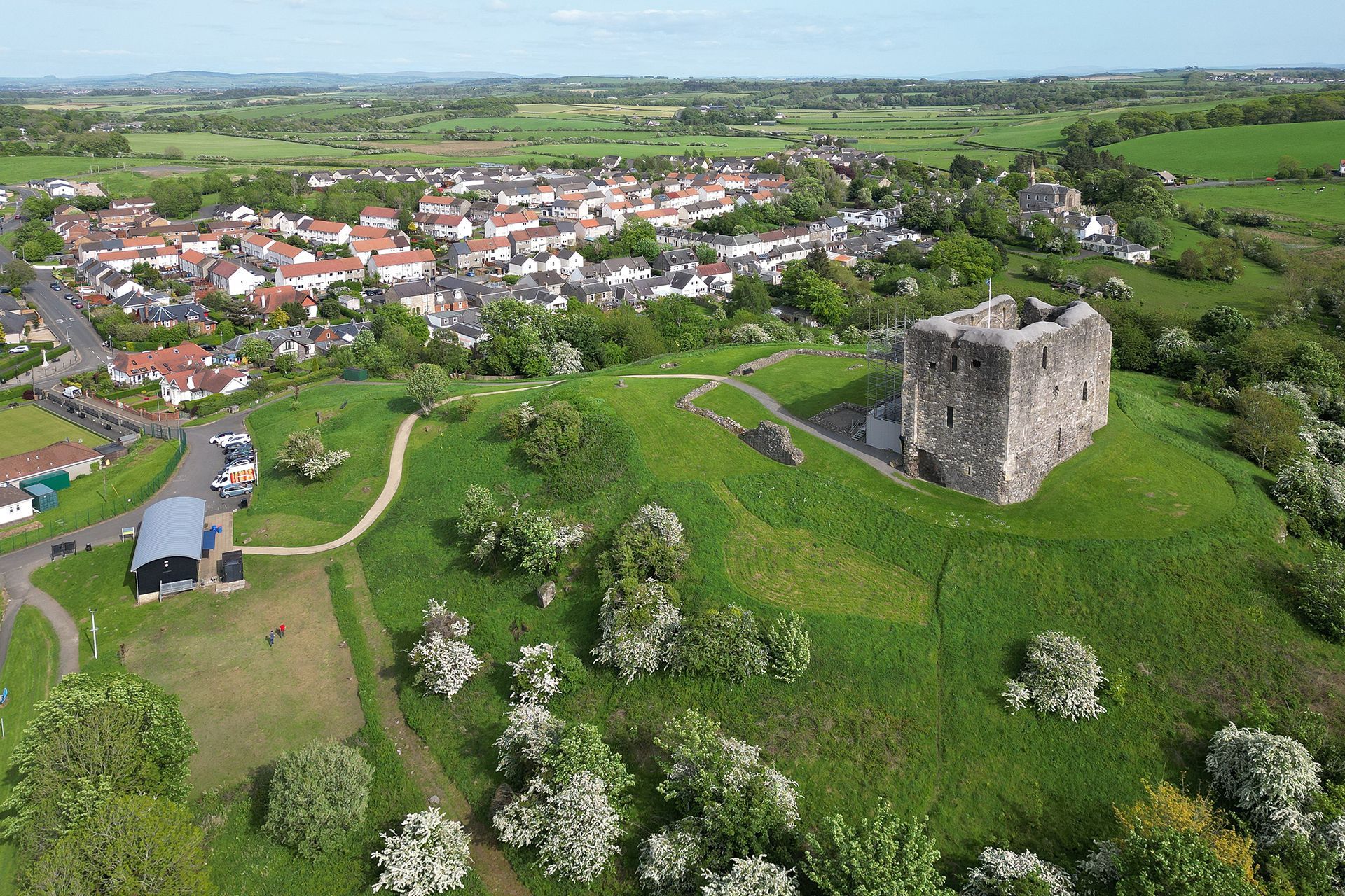 Aerial view of a green hillside with castle ruins overlooking a village and fields