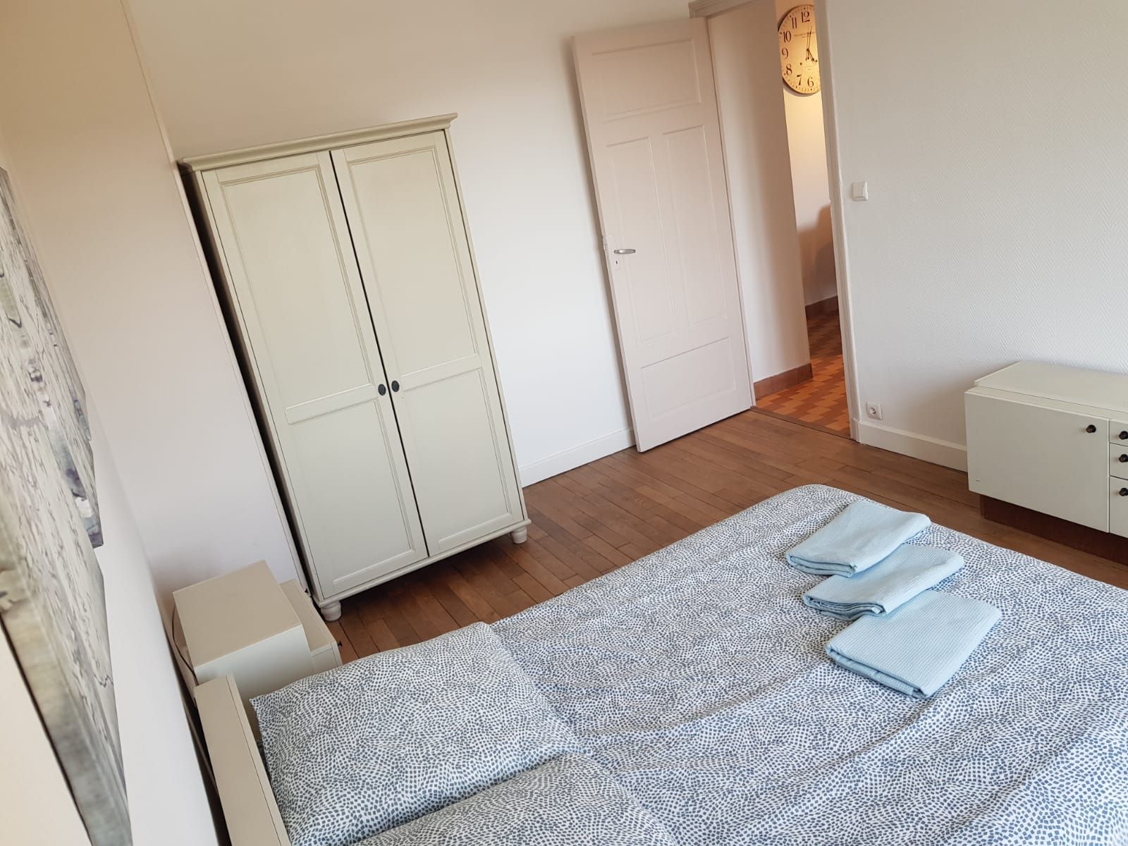 Une chambre avec des meubles de couleur claire, comprenant une armoire et un lit avec une literie à motifs bleus, et une porte ouverte.