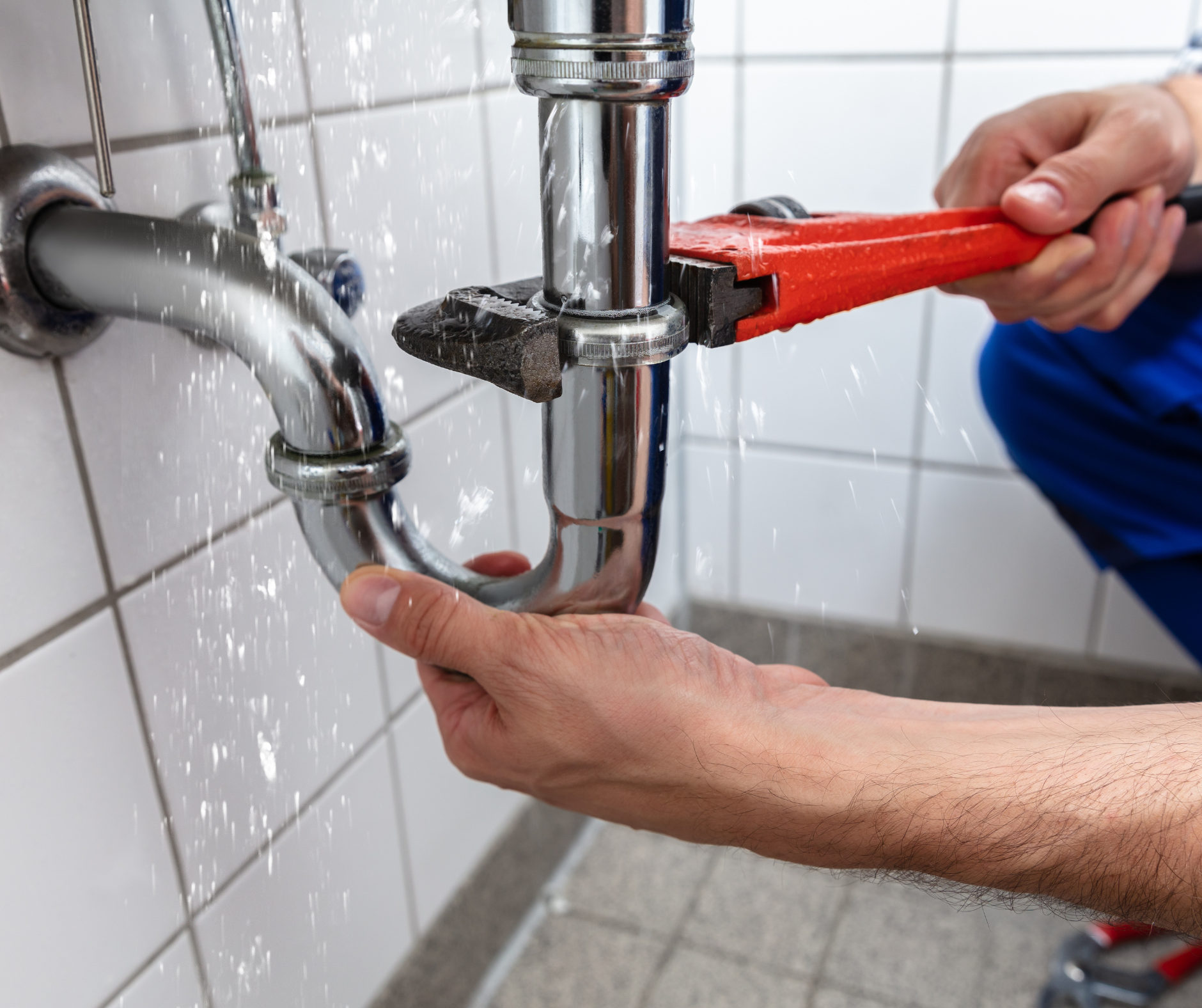 Plumber repairs a leaking chrome drainpipe with a wrench in a tiled bathroom.