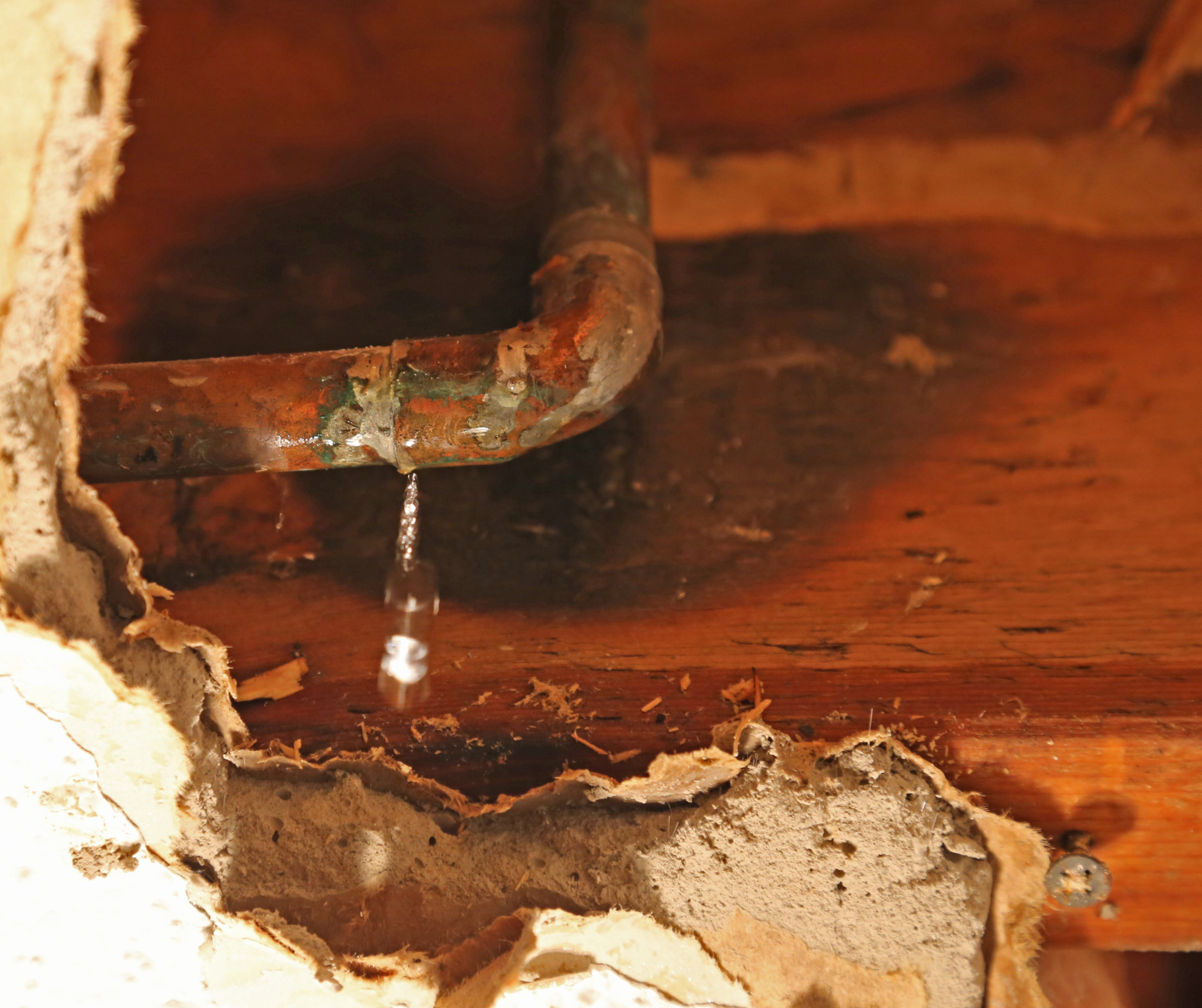 Leaking copper pipe with water droplet. Hole in the wall reveals water damage and mold.