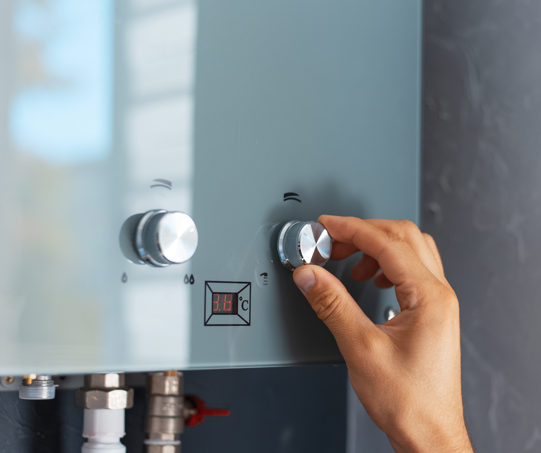 Person's hand turning a knob on a silver water heater; digital display shows temperature.