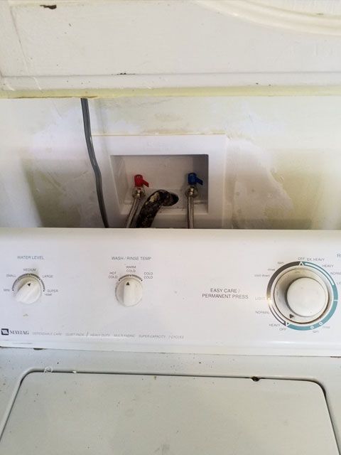 Washing machine with water hookups above. Red and blue valves visible.