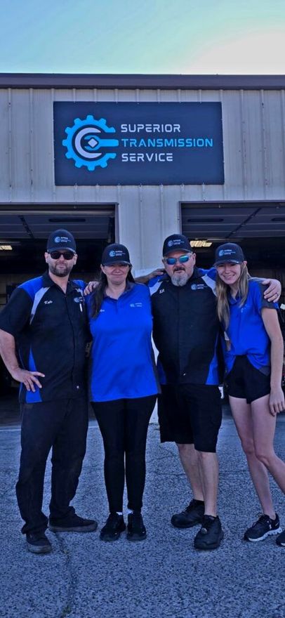 Four people in blue-and-black team shirts pose outside a building with a sign overhead | Superior Transmission Service LLC