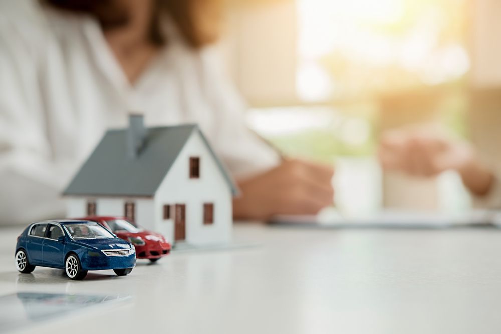 Miniature House and Cars on a Table With a Person in the Background Writing — SSP Insurance In Mackay, QLD