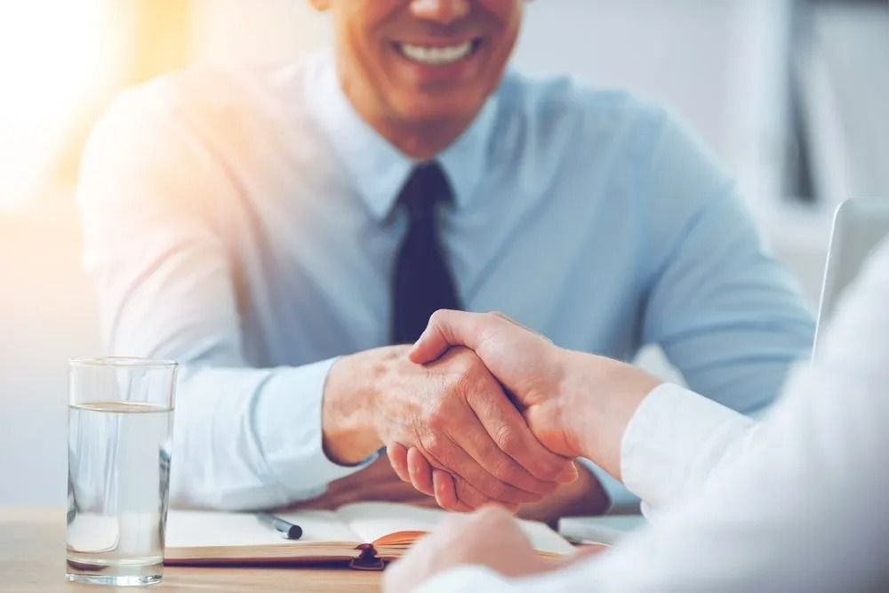 Two Men Shaking Hands Across a Desk; One Smiles — SSP Insurance In Rockhampton City, QLD
