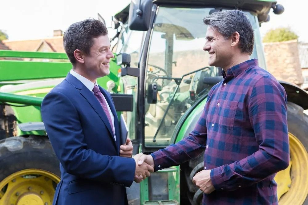 Two Men Shaking Hands Near a Green Tractor — SSP Insurance In Rockhampton City, QLD