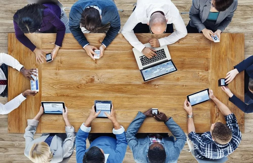 People Around a Wooden Table While Using Tablets and Phones — SSP Insurance In Rockhampton City, QLD