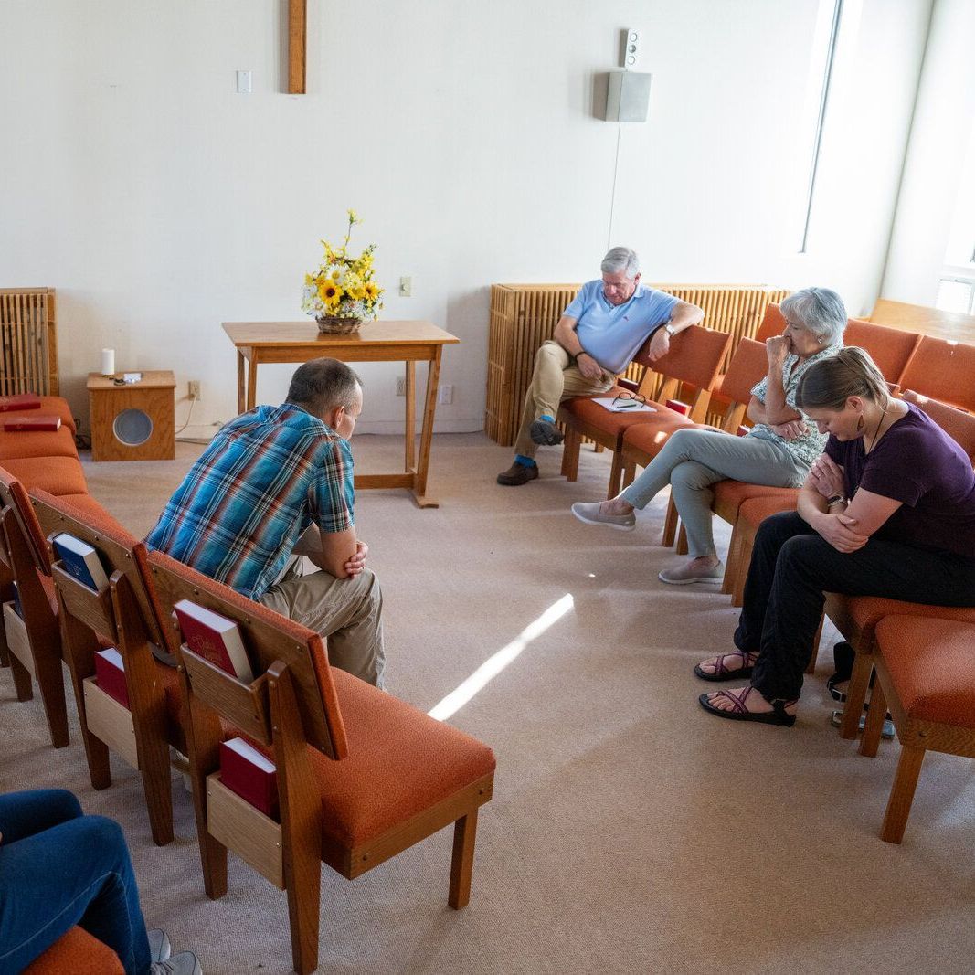A quiet moment in the Sangrey Chapel as four people sit in a semi-circle of chairs praying with their heads down.