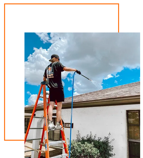 A man is standing on a ladder holding a hose in front of a house.