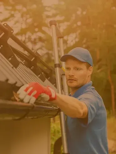 A man is cleaning a gutter on a roof with a ladder.