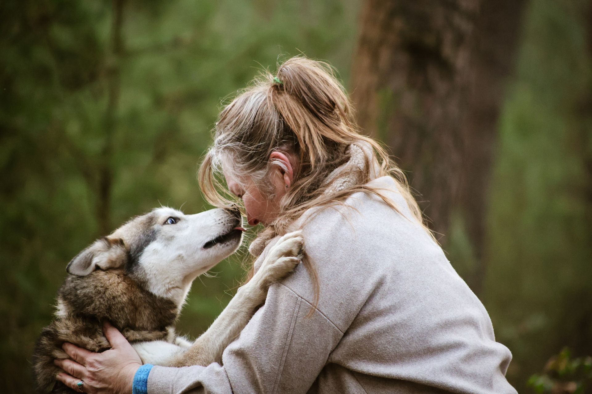 Vrouw die buiten in een bosrijke omgeving met een husky knuffelt.