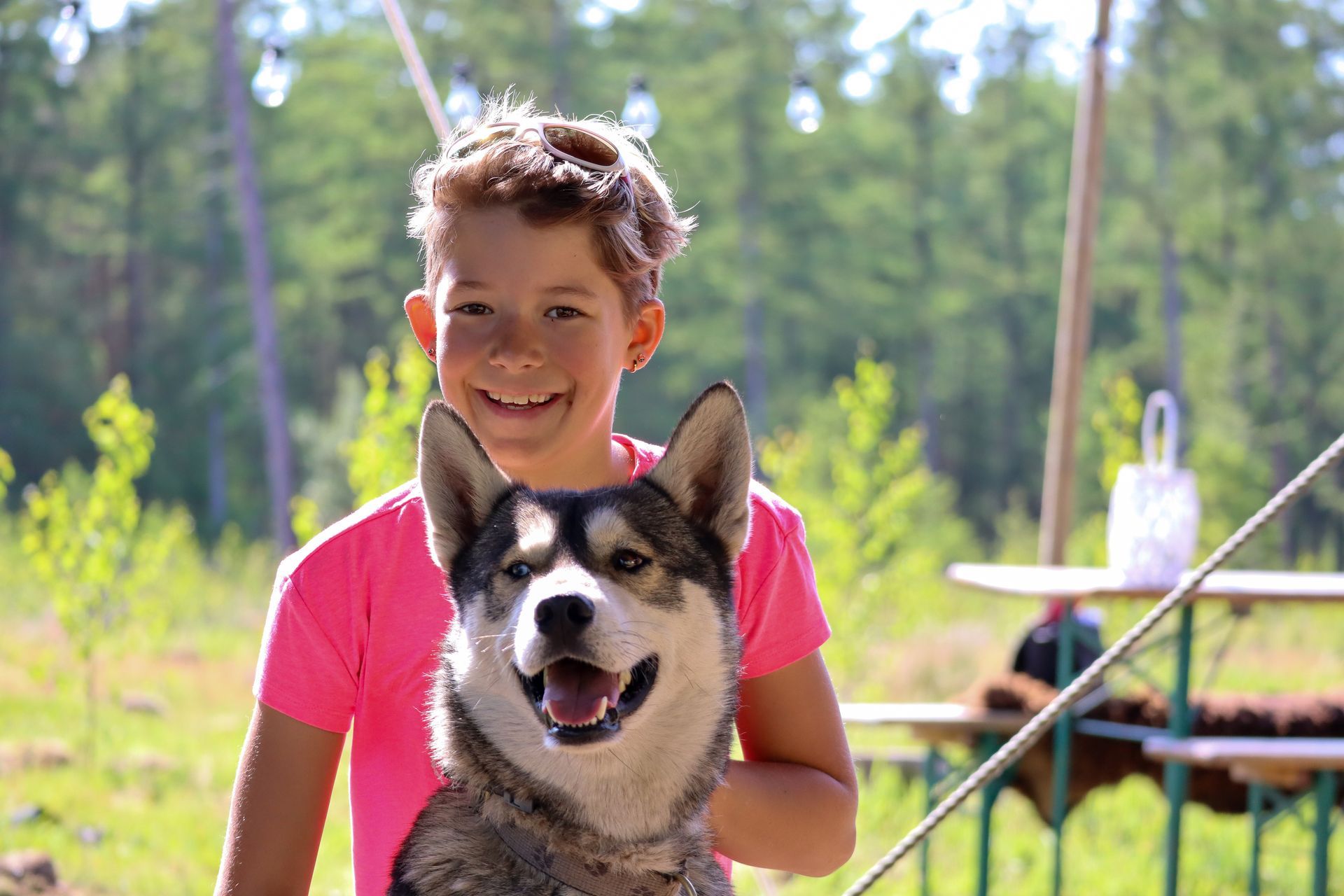 Jongen in roze shirt lacht met huskyhond buiten op zonnige dag.