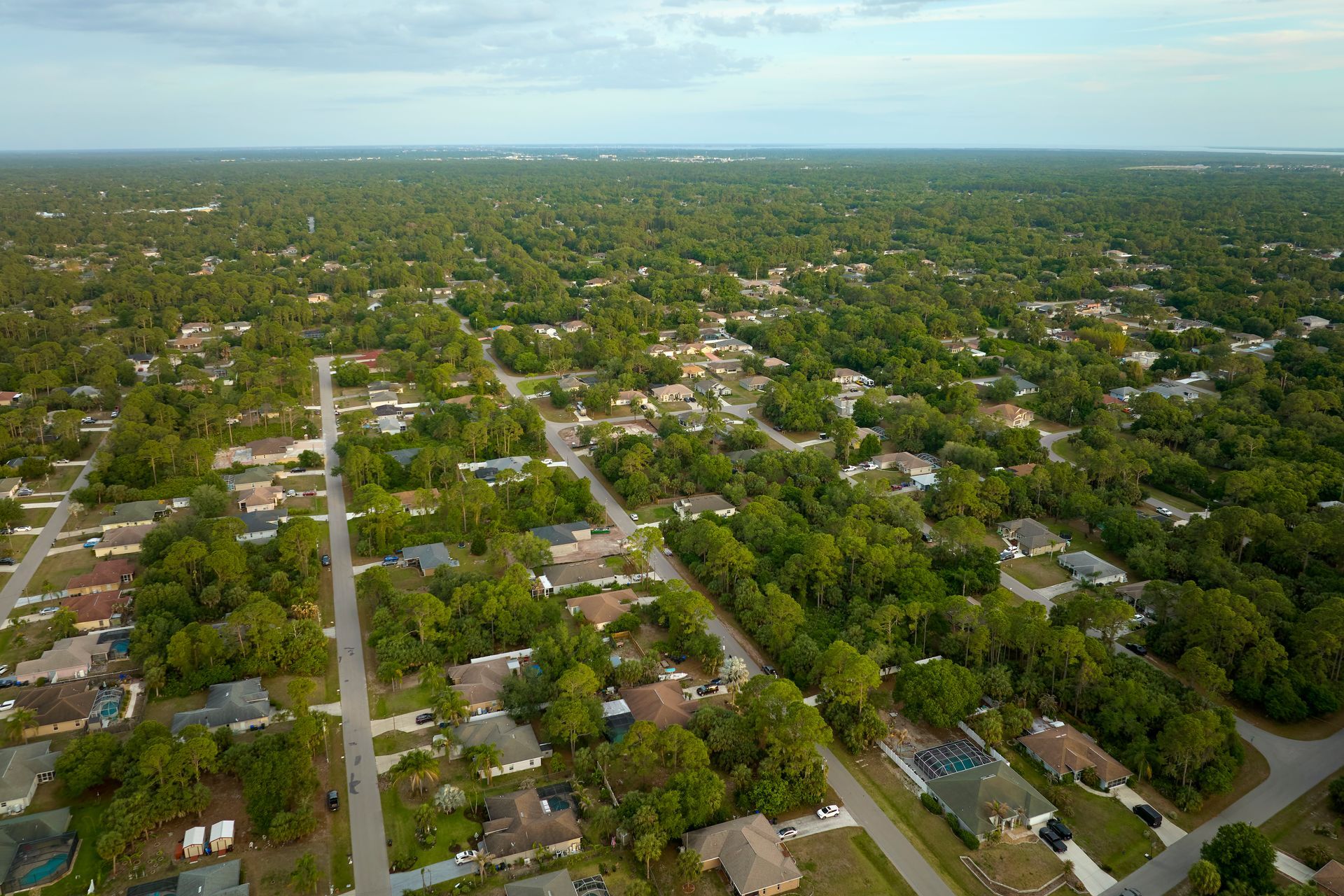Aerial view of a tree-lined suburban neighborhood with houses and streets under a clear sky
