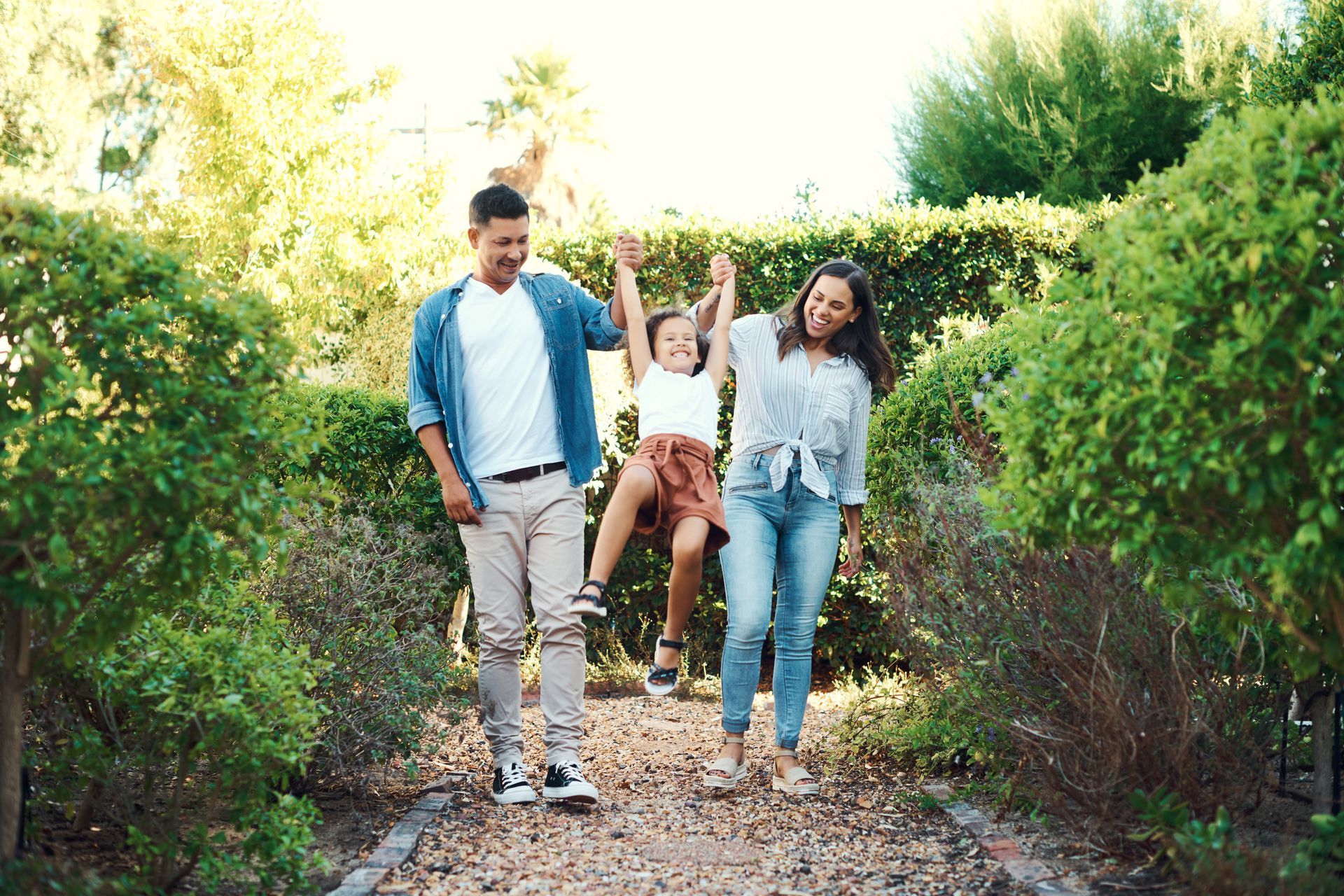 Three friends walking on a leafy garden path, smiling and holding hands.