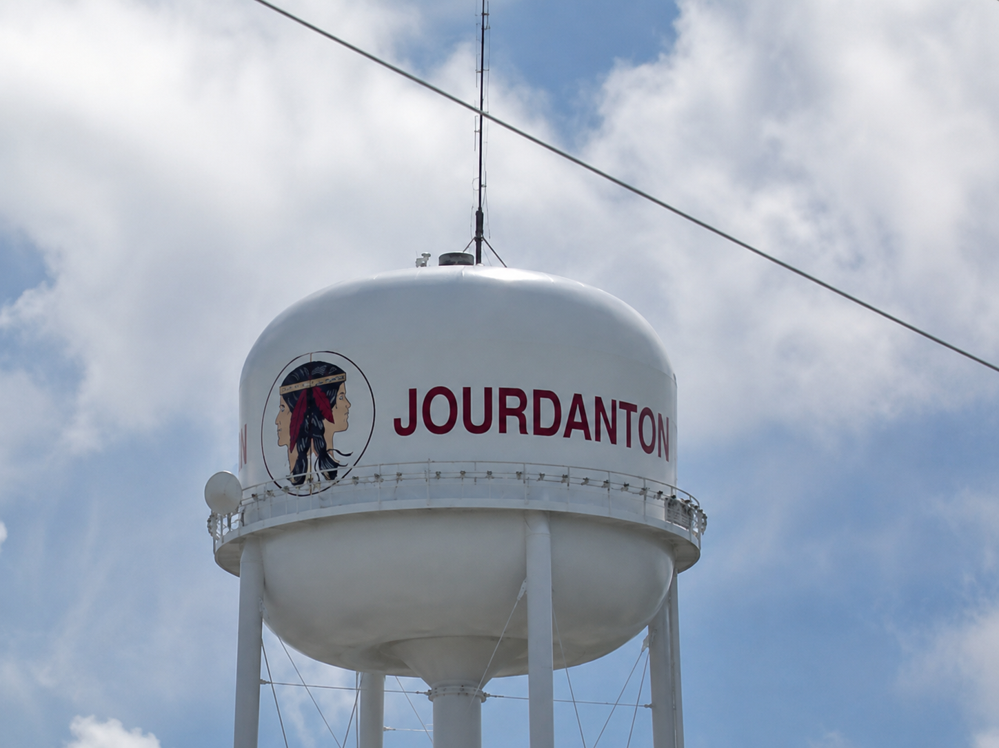 White water tower with red “JOURDANTON” lettering against a cloudy sky