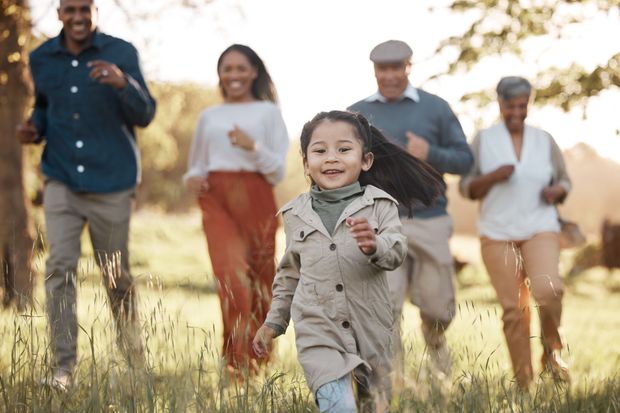 Family running through a grassy field on a sunny day, smiling and holding papers.