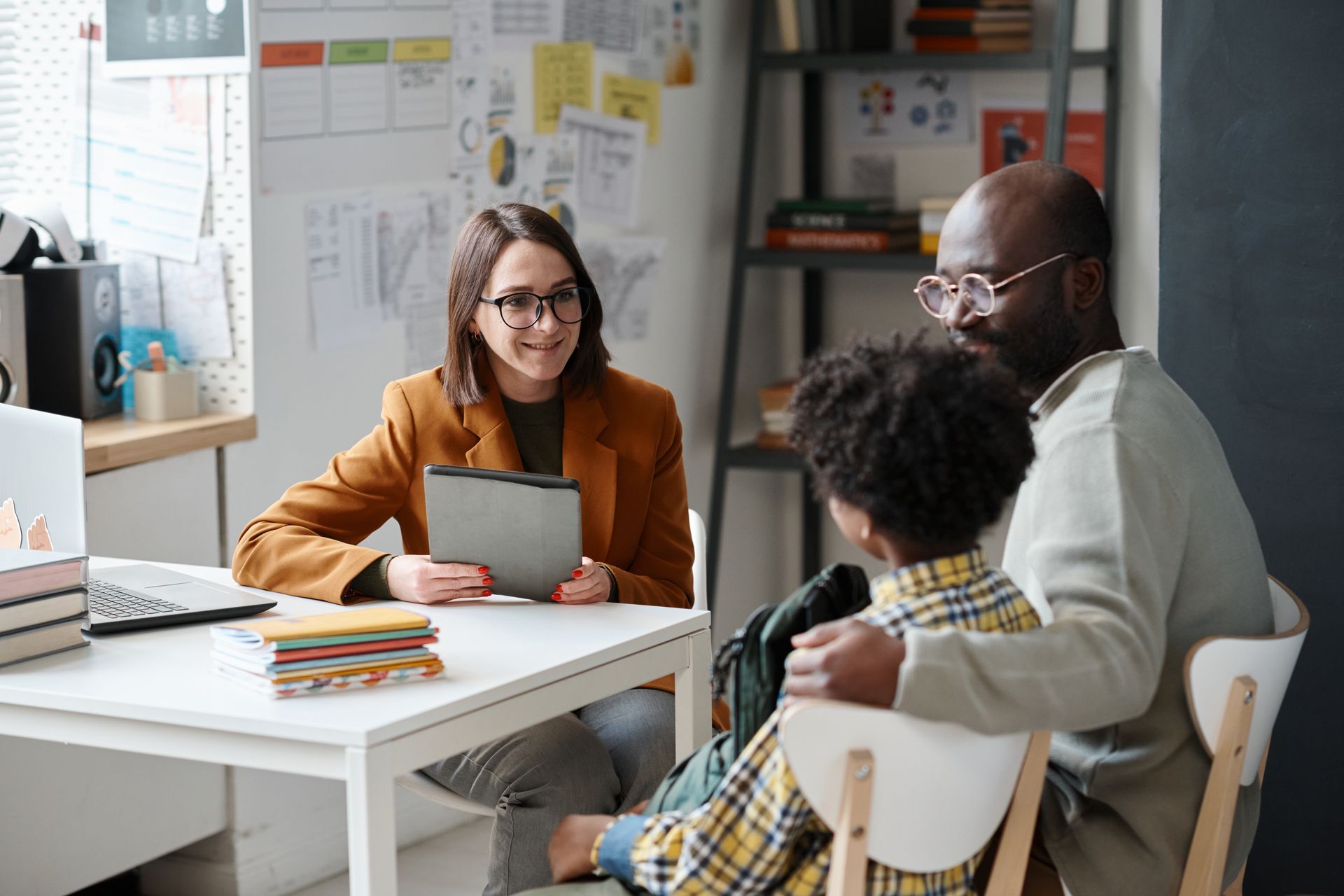 Three people in a bright office meeting, one woman holding a tablet across from a man and child.