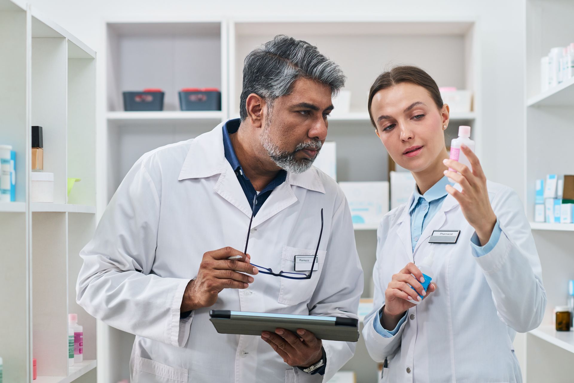 Two lab technicians in white coats discussing a tablet in a bright laboratory