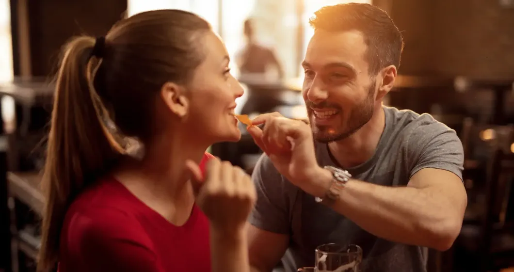A man is feeding a woman french fries in a restaurant.