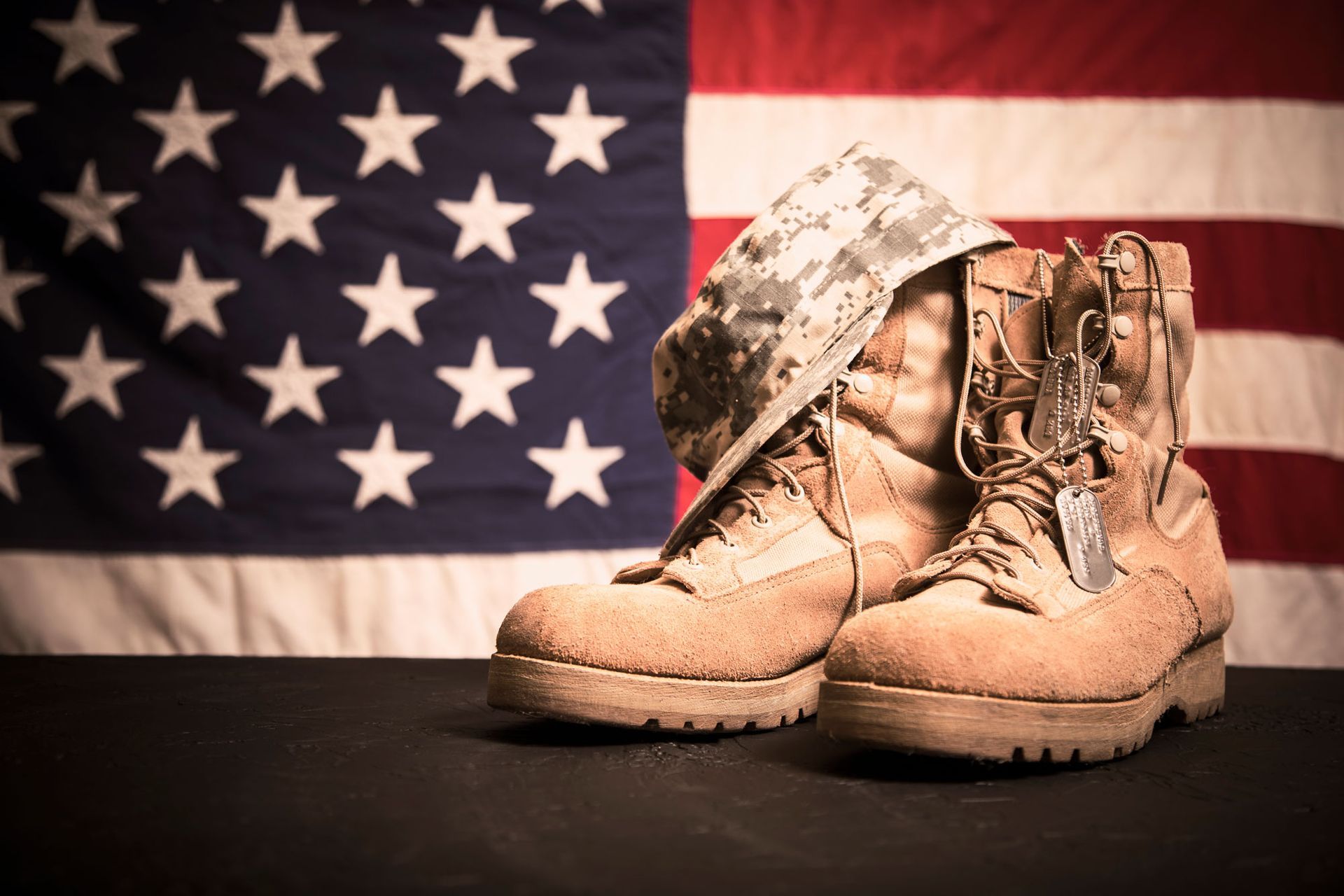 A pair of military boots and a helmet are sitting in front of an american flag.