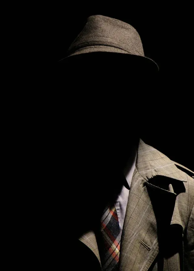 A man in a suit and hat is standing in the dark.