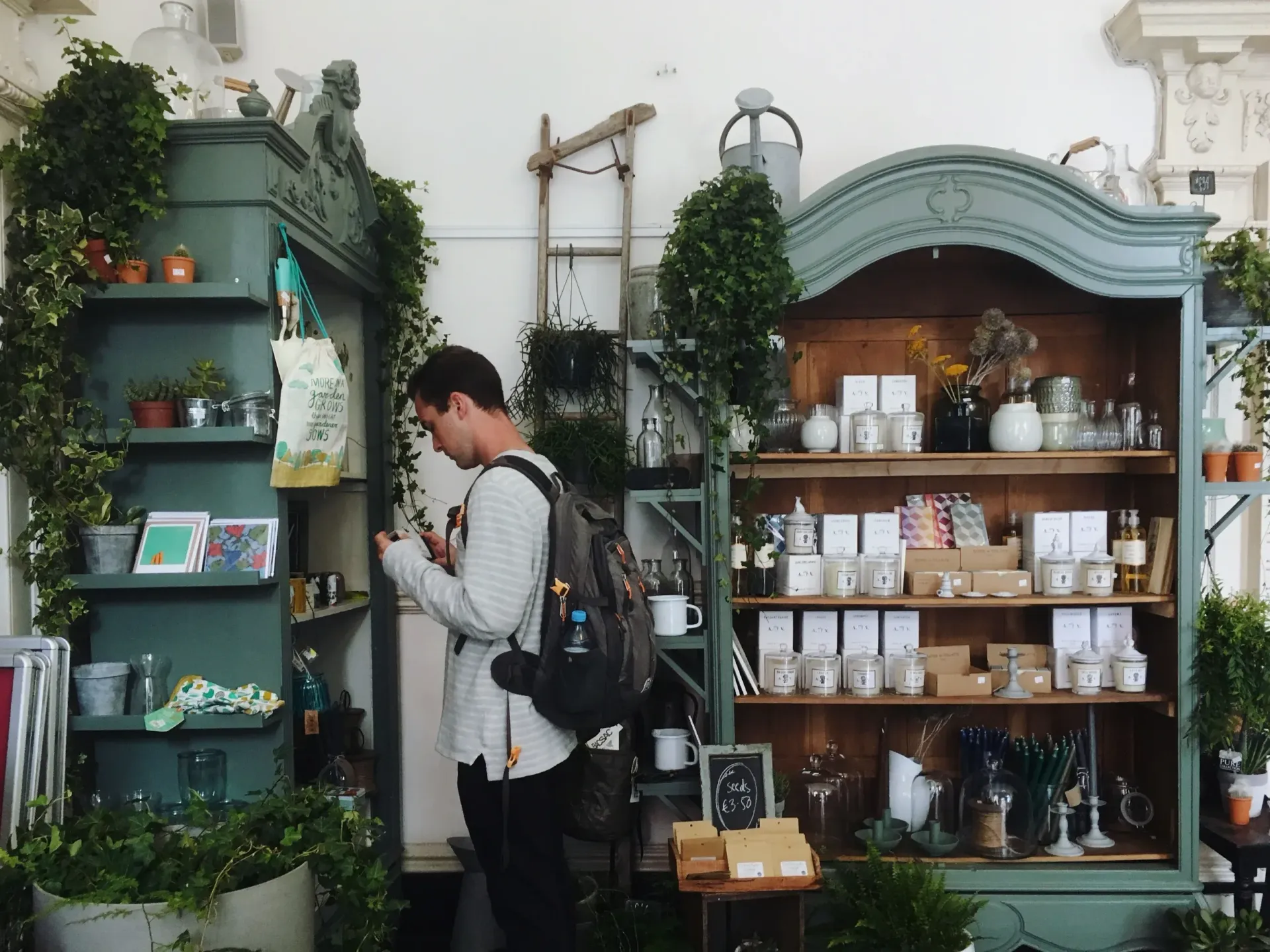 A man with a backpack is looking at his phone in a store.