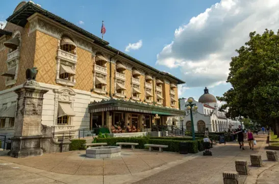 A large building with a lot of windows is surrounded by trees and a sidewalk.