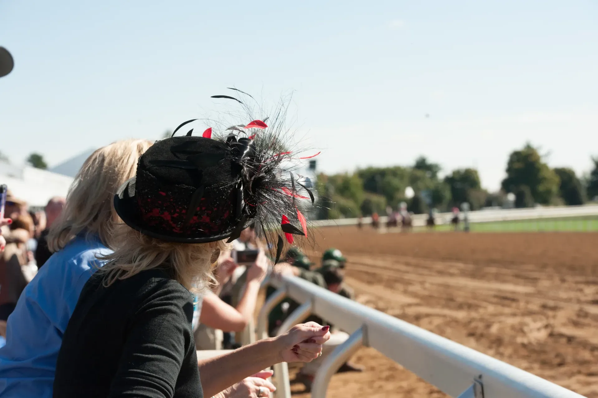 A woman in a black hat is watching a horse race.