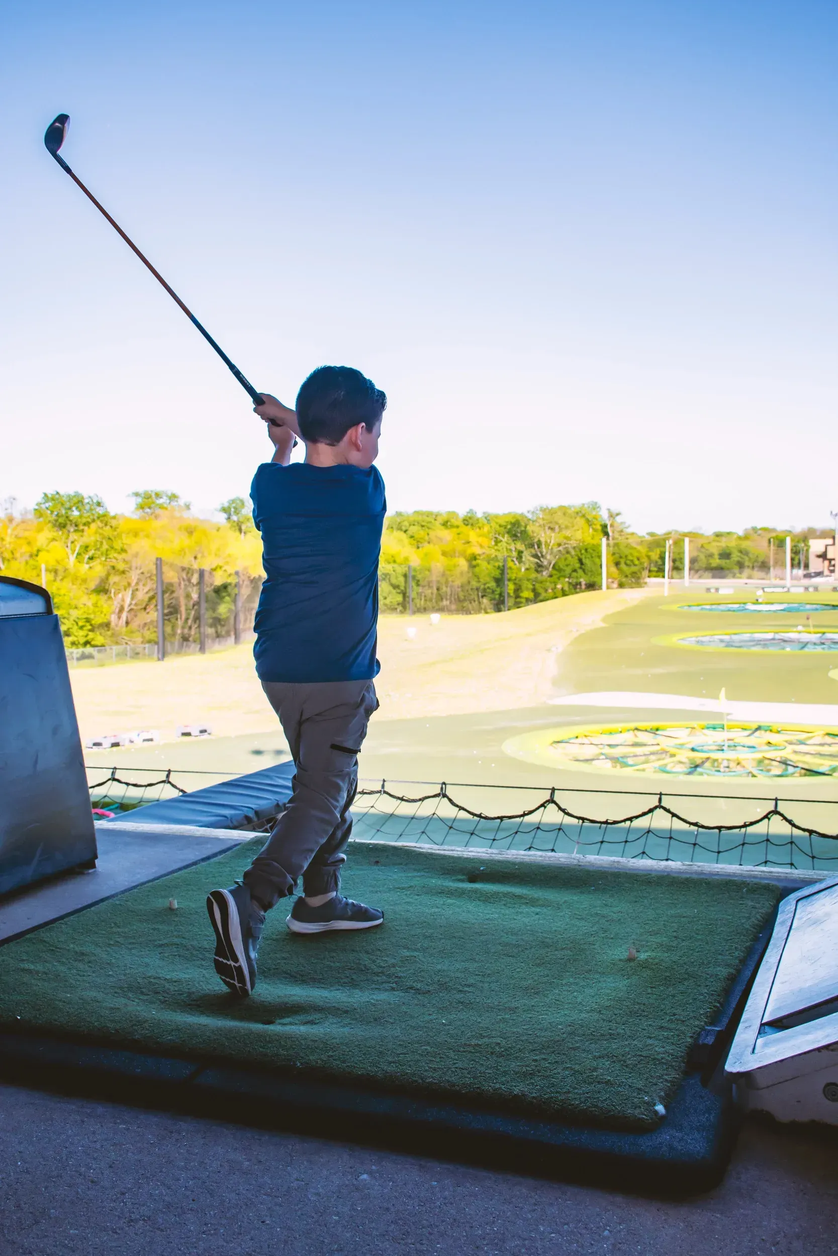 A young boy is swinging a golf club on a driving range.