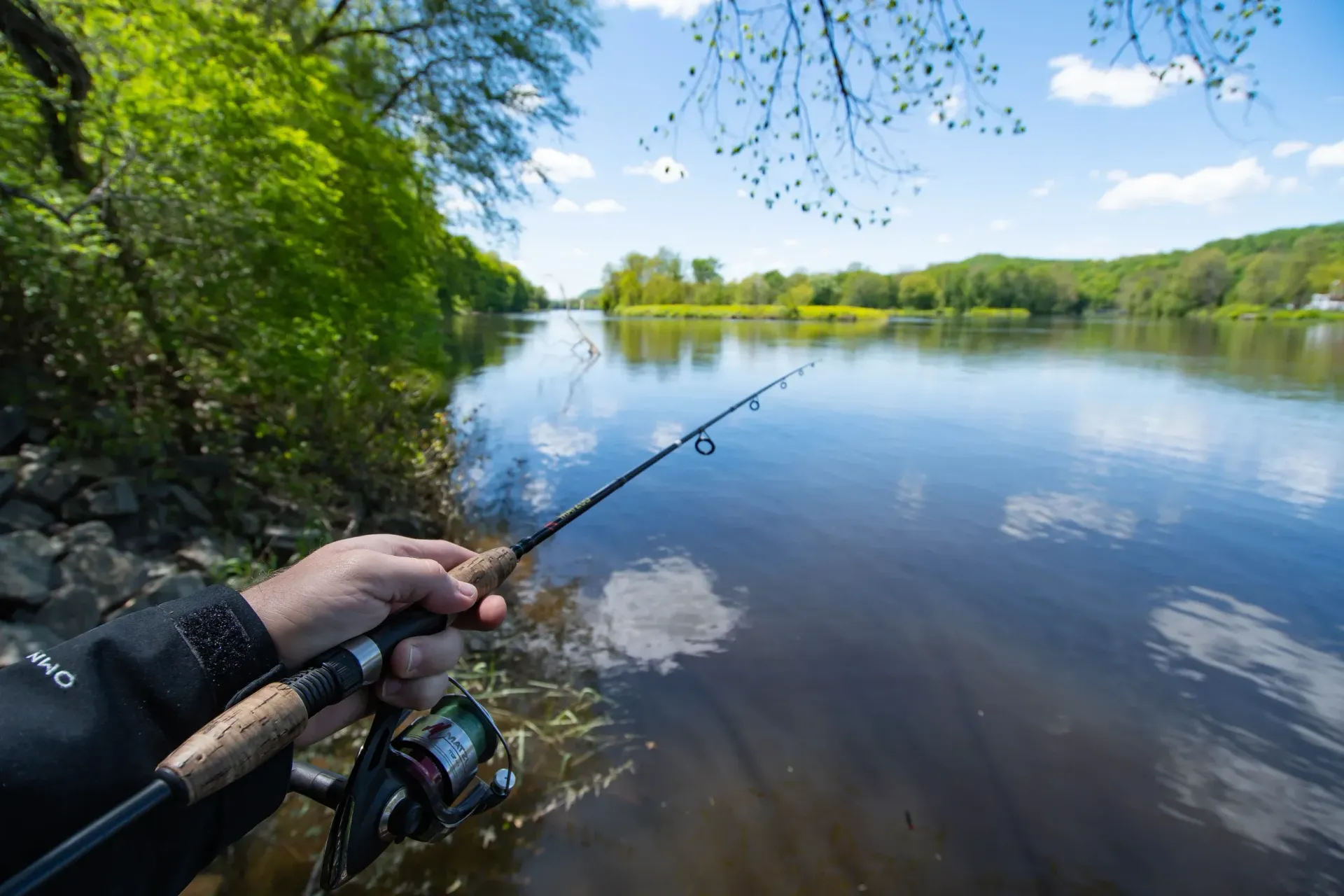 A person is holding a fishing rod in front of a lake.