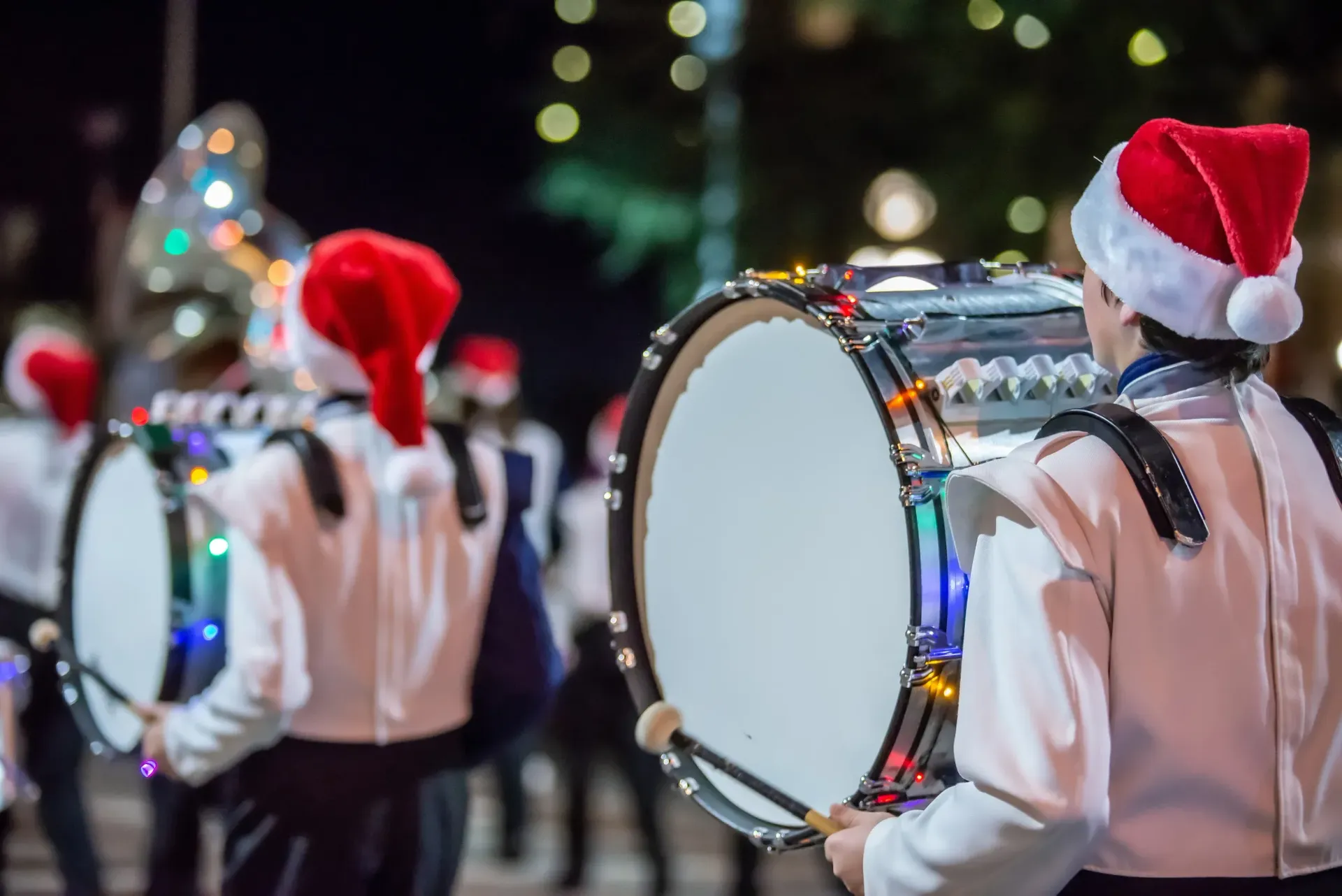 A group of people wearing santa hats are playing drums in a marching band.