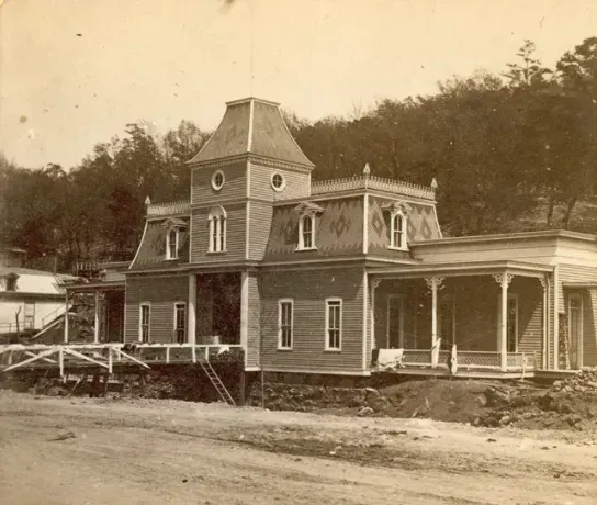 A black and white photo of a large house with a tower and porch.