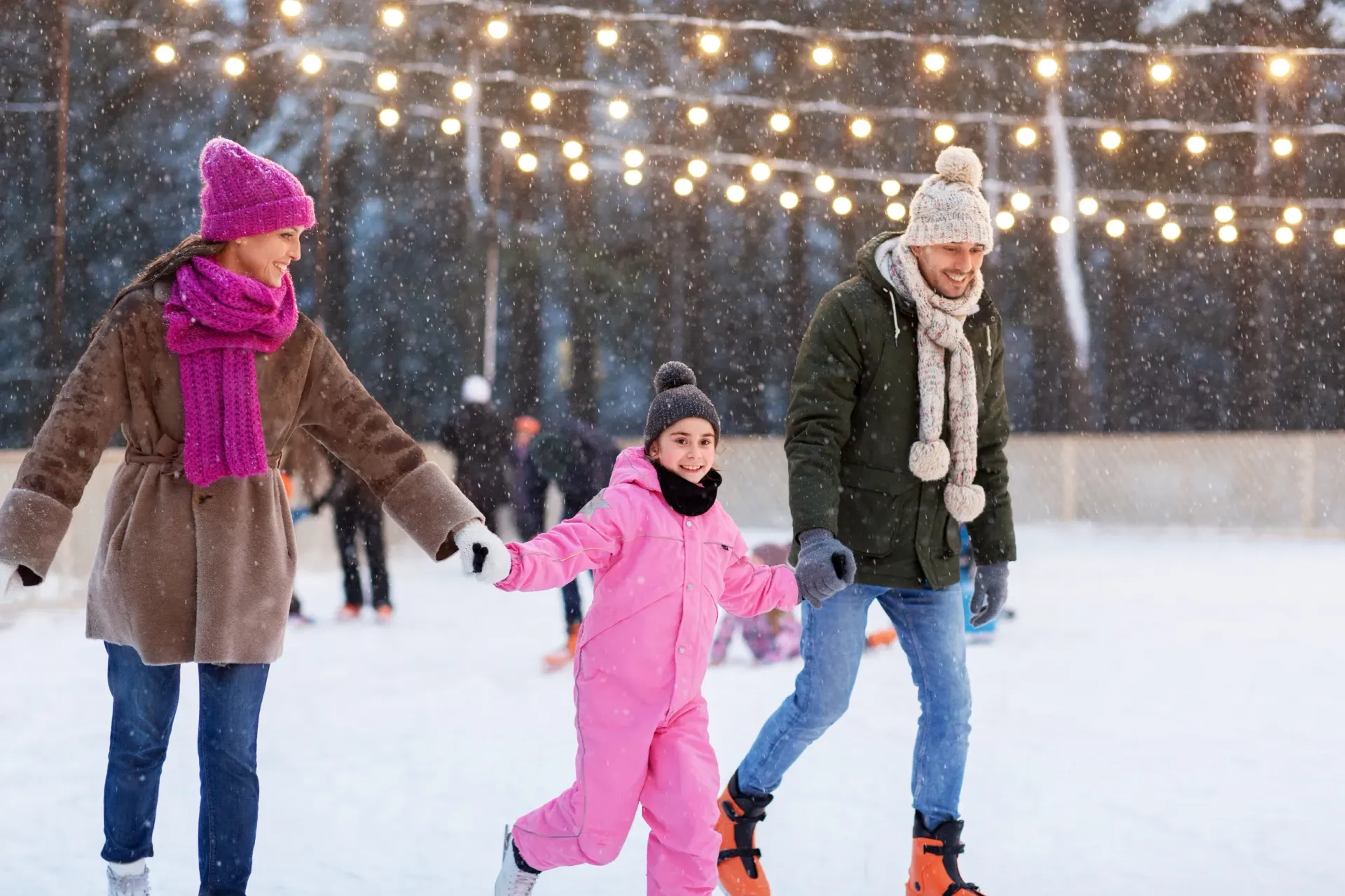 A family is holding hands while ice skating on a rink.