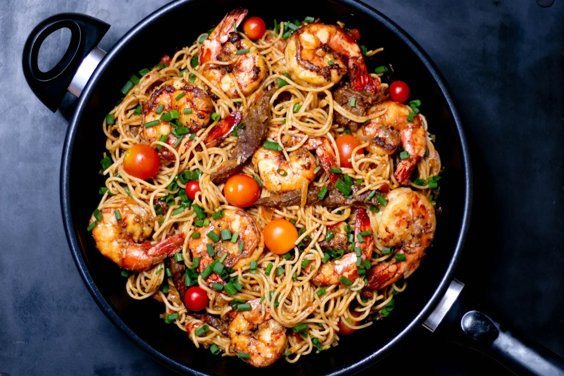 A pan filled with noodles , shrimp and tomatoes.