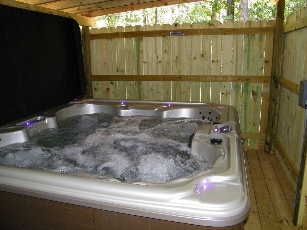 A hot tub is sitting under a wooden fence.