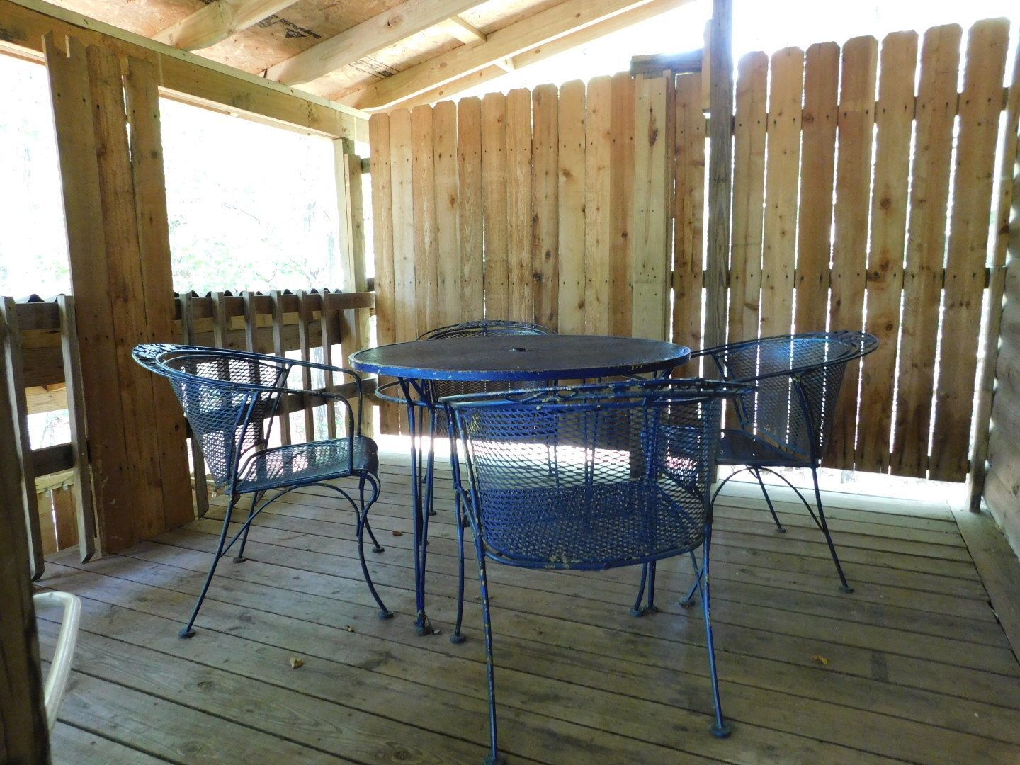 A table and chairs on a wooden deck with a wooden fence in the background.