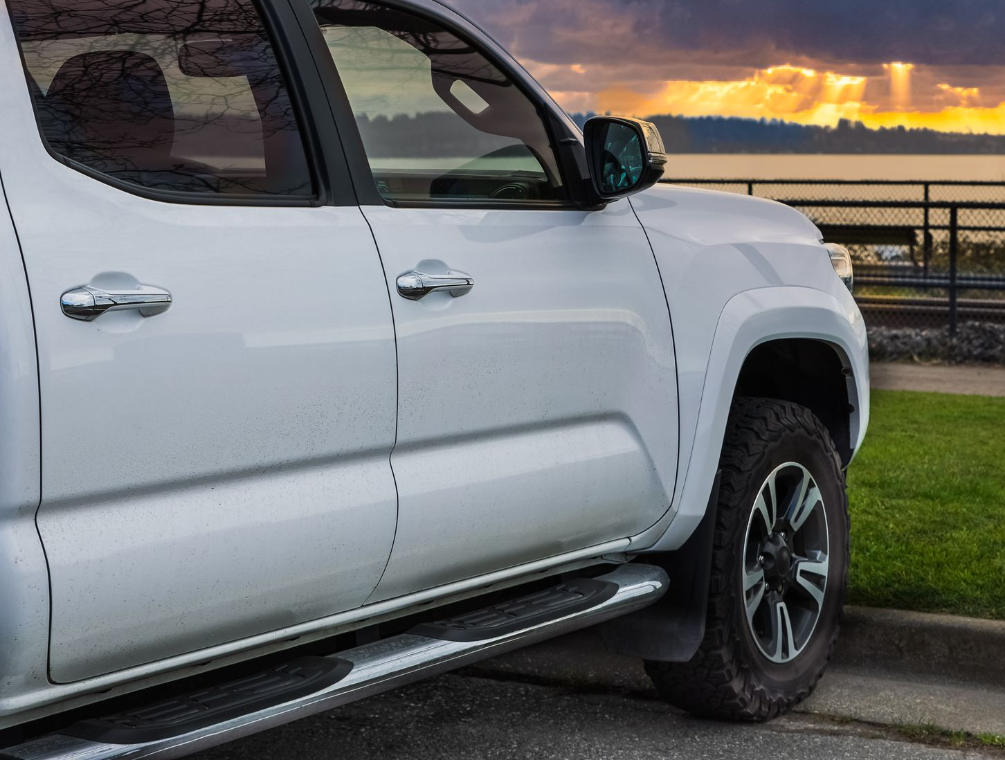 White pickup truck parked by a curb at sunset near water and a railing